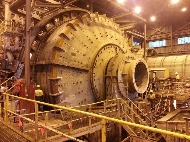 Massive riveted industrial rotor being worked on inside a factory, with workers and safety railing around it at a manufacturing site.